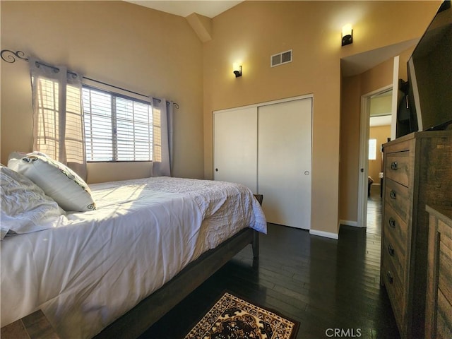 bedroom with dark hardwood / wood-style floors, lofted ceiling, and a closet