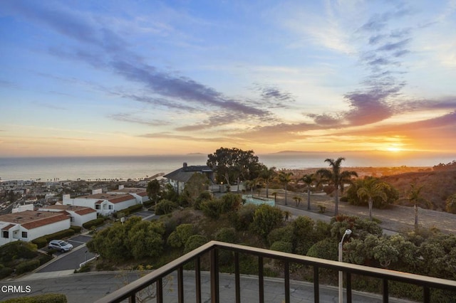 balcony at dusk featuring a water view