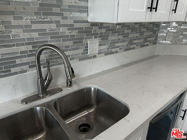 interior details with white cabinets, decorative backsplash, light stone countertops, and sink