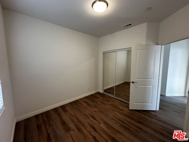 unfurnished bedroom with dark hardwood / wood-style flooring and a closet