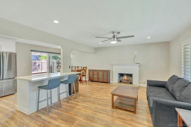 living room featuring light wood-type flooring, a brick fireplace, and ceiling fan