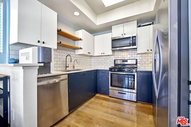 kitchen featuring appliances with stainless steel finishes, light wood-type flooring, blue cabinets, sink, and white cabinetry