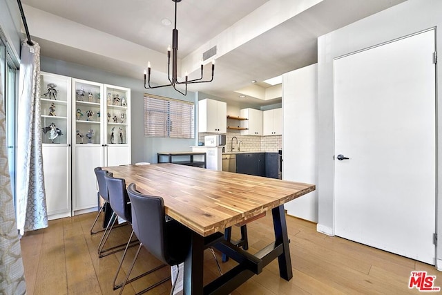 dining area featuring light wood-type flooring, a notable chandelier, and sink