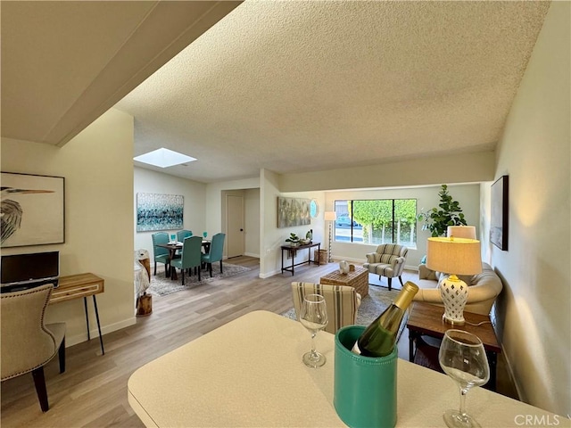 living room featuring a skylight, a textured ceiling, baseboards, and wood finished floors