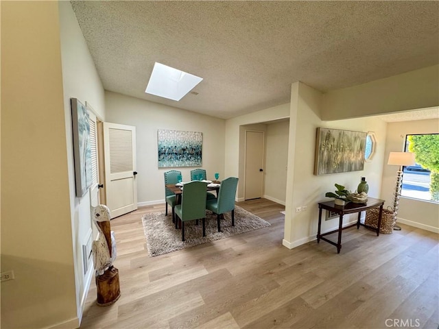 dining area with a textured ceiling, vaulted ceiling with skylight, wood finished floors, and baseboards