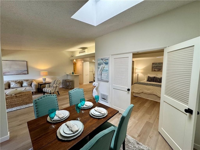 dining space with a skylight, light wood-style flooring, visible vents, and a textured ceiling