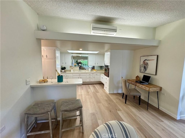 kitchen featuring light countertops, oven, a wall unit AC, and white cabinetry