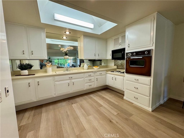 kitchen with a skylight, wall oven, white cabinets, a sink, and black microwave