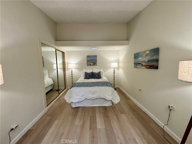 bedroom featuring a textured ceiling, a closet, baseboards, and wood finished floors