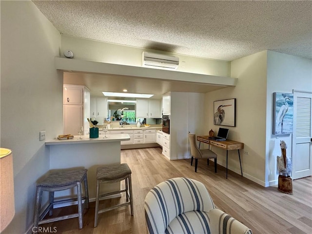 kitchen with light countertops, white cabinets, a wall unit AC, and light wood-style flooring