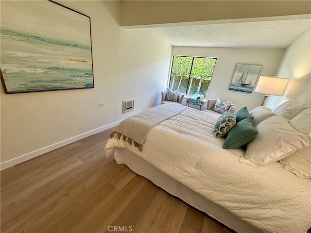 bedroom with a textured ceiling, wood finished floors, visible vents, and baseboards