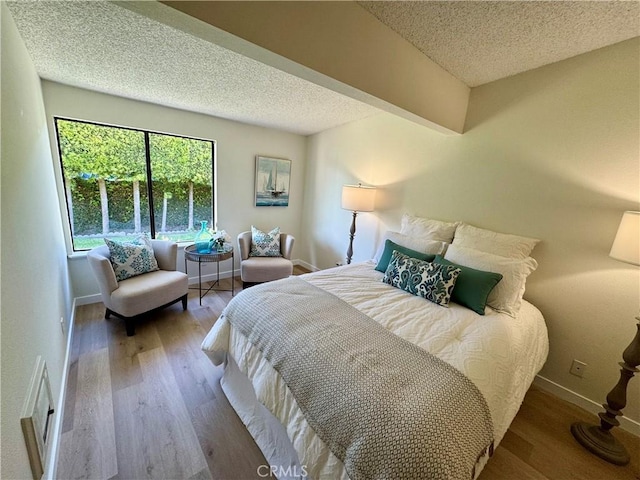 bedroom with a textured ceiling, baseboards, and wood finished floors