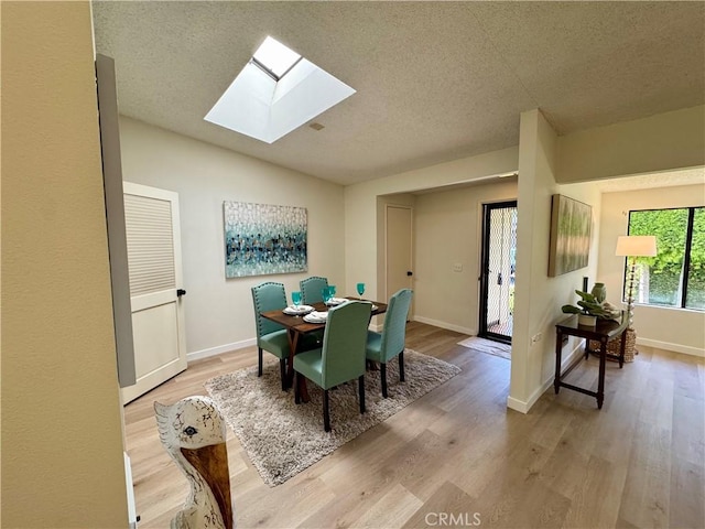 dining area with lofted ceiling with skylight, light wood-style flooring, baseboards, and a textured ceiling