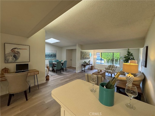 living room with lofted ceiling with skylight, baseboards, light wood-style flooring, and a textured ceiling