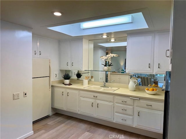 kitchen featuring light countertops, white cabinets, a sink, and freestanding refrigerator