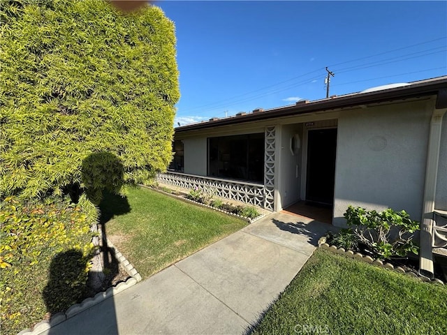 doorway to property featuring a lawn and stucco siding