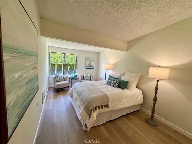 bedroom featuring a textured ceiling, baseboards, and wood finished floors