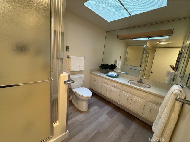 bathroom featuring wood finished floors, a stall shower, vanity, and toilet