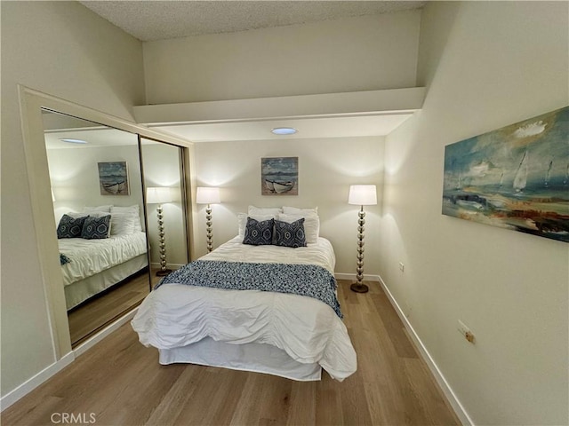 bedroom featuring a closet, a textured ceiling, baseboards, and wood finished floors