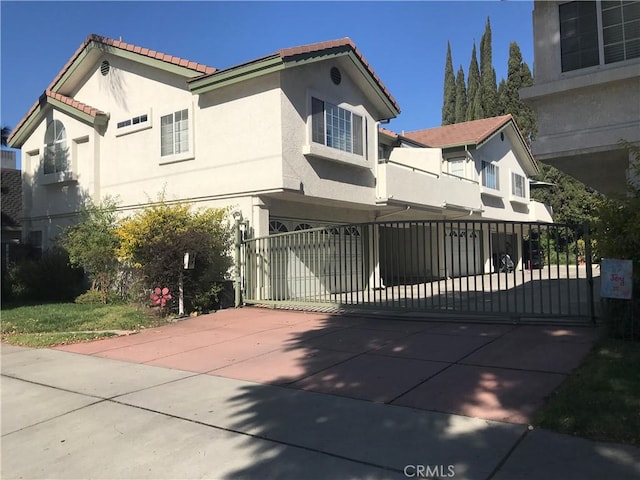 exterior space with an attached garage, driveway, a tiled roof, a gate, and stucco siding