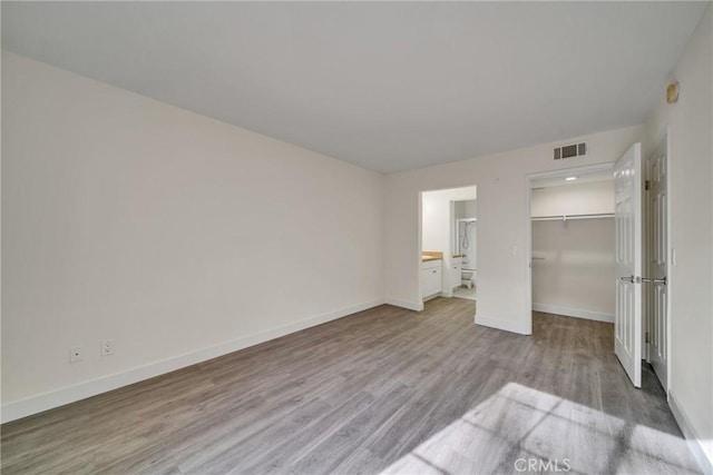 unfurnished bedroom featuring connected bathroom, a closet, light hardwood / wood-style flooring, and a spacious closet