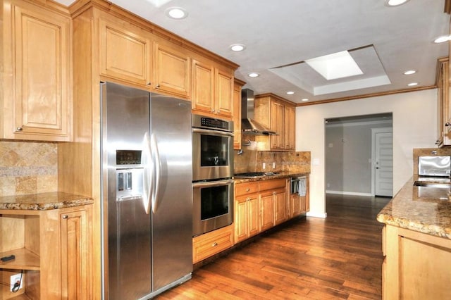 kitchen featuring a skylight, stainless steel appliances, a raised ceiling, light stone countertops, and wall chimney exhaust hood