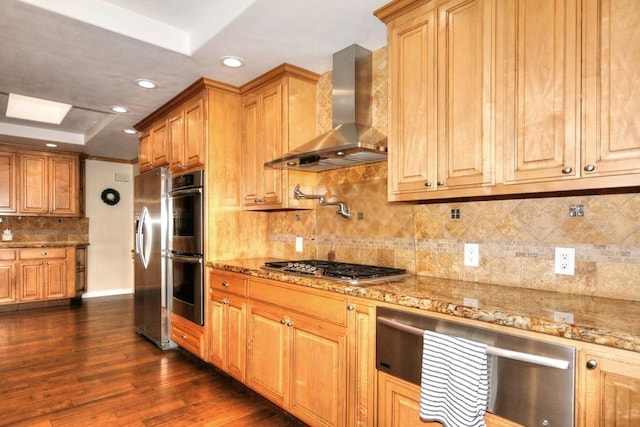 kitchen featuring appliances with stainless steel finishes, tasteful backsplash, dark wood-type flooring, light stone countertops, and wall chimney range hood