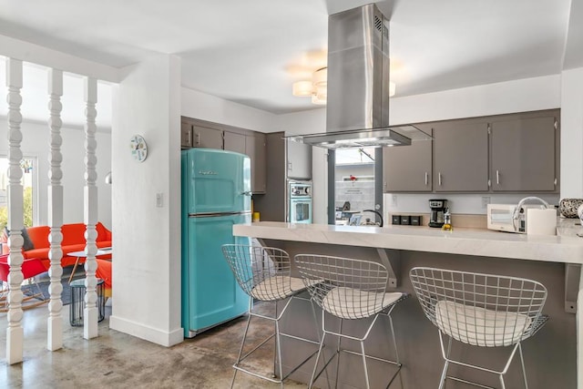 kitchen with kitchen peninsula, appliances with stainless steel finishes, island range hood, and a kitchen breakfast bar