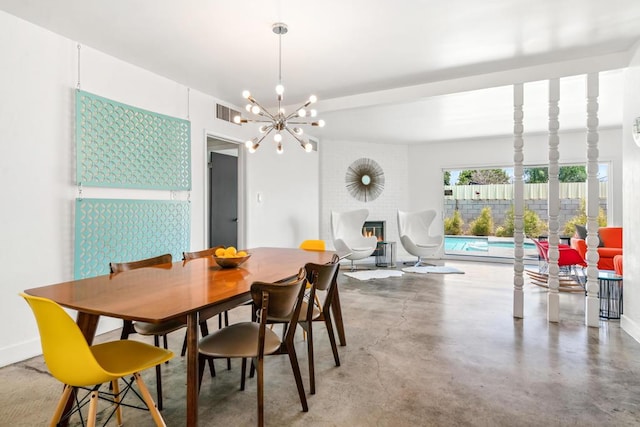 dining area featuring a chandelier, concrete flooring, and a brick fireplace