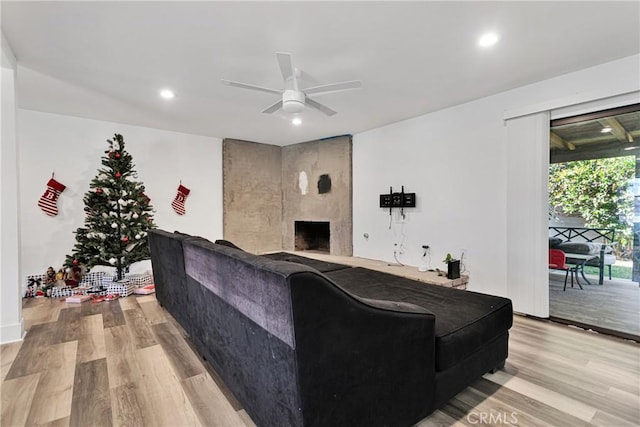 living room with ceiling fan, a large fireplace, and light hardwood / wood-style flooring