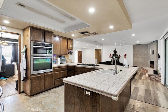 kitchen featuring a fireplace, kitchen peninsula, sink, tile counters, and ceiling fan with notable chandelier