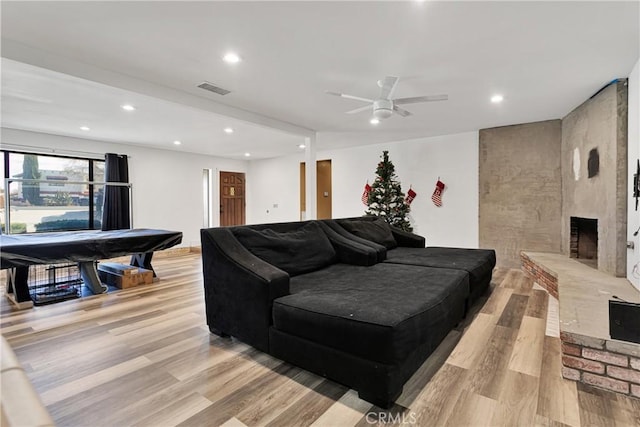 living room featuring ceiling fan, a large fireplace, and light hardwood / wood-style floors