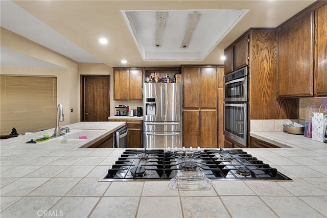 kitchen featuring stainless steel appliances, tile counters, a tray ceiling, ornamental molding, and sink