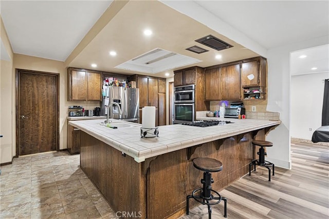 kitchen with a kitchen bar, kitchen peninsula, tile counters, stainless steel appliances, and sink