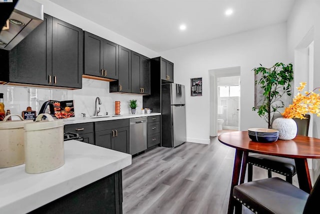 kitchen featuring sink, light hardwood / wood-style flooring, backsplash, exhaust hood, and appliances with stainless steel finishes