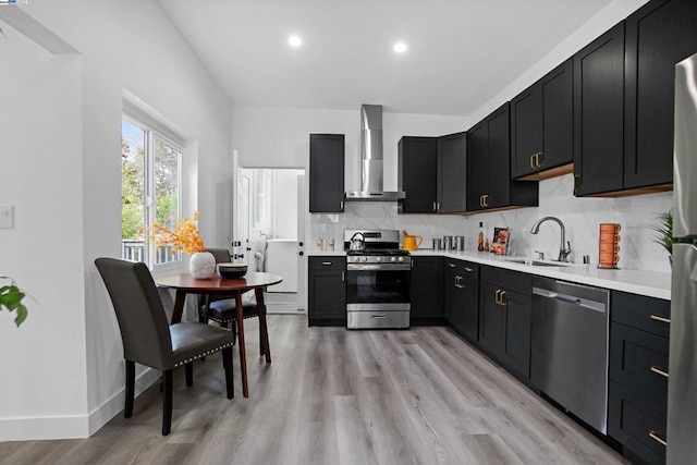 kitchen with sink, wall chimney exhaust hood, decorative backsplash, appliances with stainless steel finishes, and light wood-type flooring