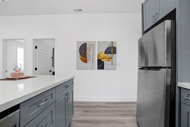 kitchen with gray cabinetry, stainless steel fridge, and light wood-type flooring