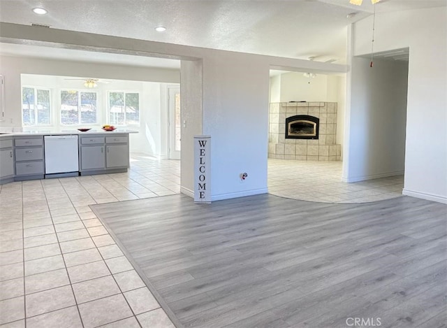 unfurnished living room with light wood-type flooring, a textured ceiling, a tile fireplace, and ceiling fan