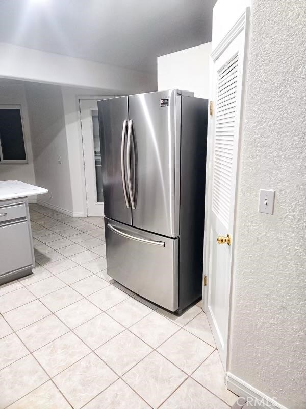 kitchen with gray cabinetry, stainless steel fridge, and light tile patterned flooring