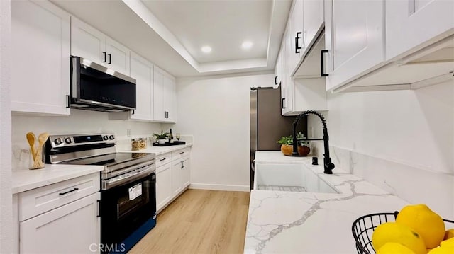 kitchen featuring white cabinetry, stainless steel appliances, sink, light stone counters, and a tray ceiling