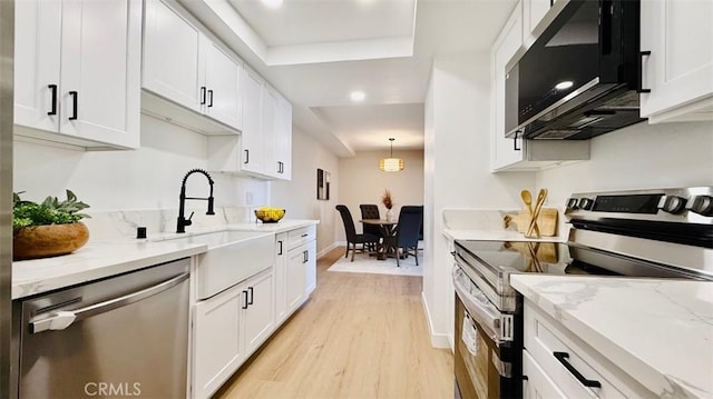 kitchen featuring appliances with stainless steel finishes, white cabinets, pendant lighting, light hardwood / wood-style flooring, and light stone counters