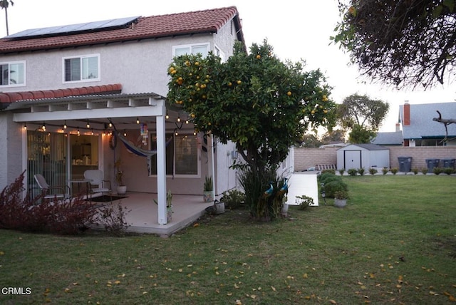 rear view of property featuring a lawn, a storage shed, solar panels, and a patio