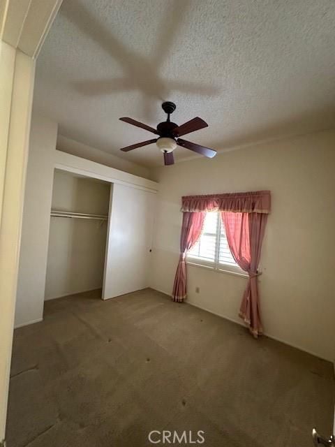 unfurnished bedroom featuring a textured ceiling, carpet floors, a closet, and ceiling fan