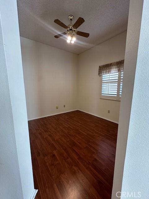 empty room with ceiling fan, dark wood-type flooring, and a textured ceiling