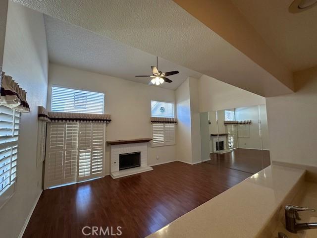 unfurnished living room featuring lofted ceiling, ceiling fan, dark hardwood / wood-style floors, and a textured ceiling