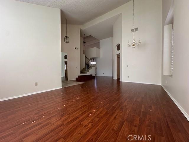 unfurnished living room with a notable chandelier, a towering ceiling, a textured ceiling, and dark hardwood / wood-style flooring