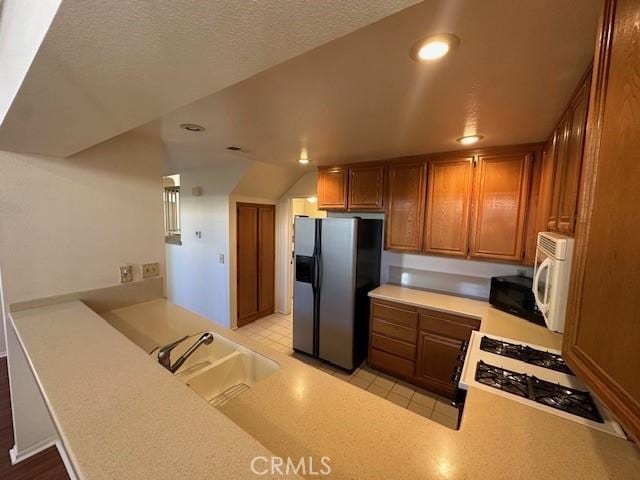 kitchen featuring sink, light tile patterned floors, white appliances, kitchen peninsula, and a textured ceiling