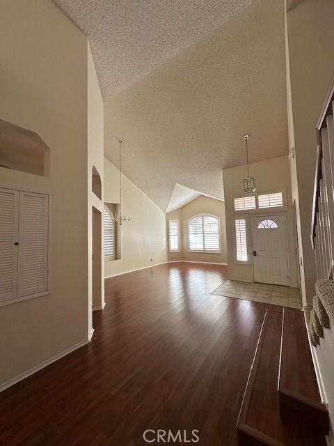 foyer entrance with hardwood / wood-style floors, a textured ceiling, high vaulted ceiling, and a notable chandelier