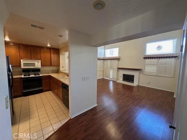 kitchen with a textured ceiling, light hardwood / wood-style flooring, white appliances, and a brick fireplace