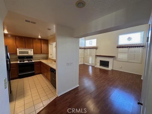 kitchen with range with gas stovetop, refrigerator, dishwasher, light hardwood / wood-style floors, and a brick fireplace